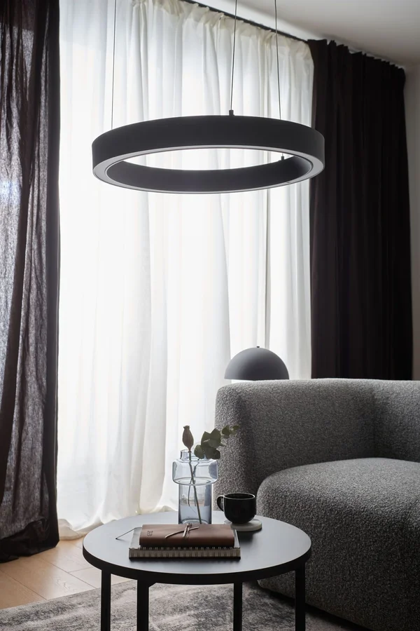 Stylowa lampa i sofa na tle ciemnych zasłon, co dodaje wnętrzu wysokości.